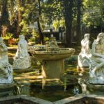 Elegant white statues encircle a fountain in a peaceful outdoor garden.