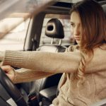Side view of concentrated contemporary female driver in casual clothes going along street road alone by car with leather interior
