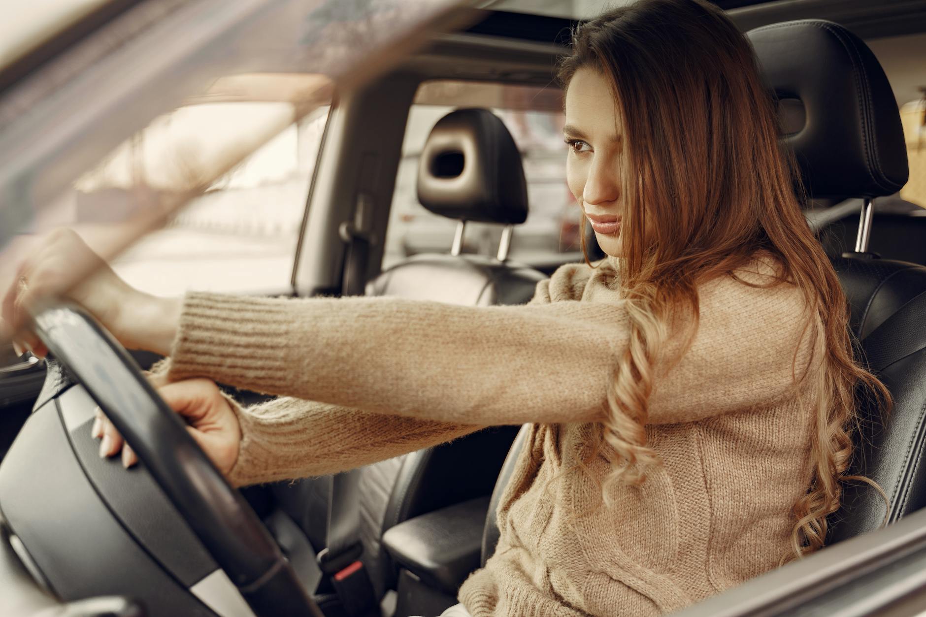 Side view of concentrated contemporary female driver in casual clothes going along street road alone by car with leather interior