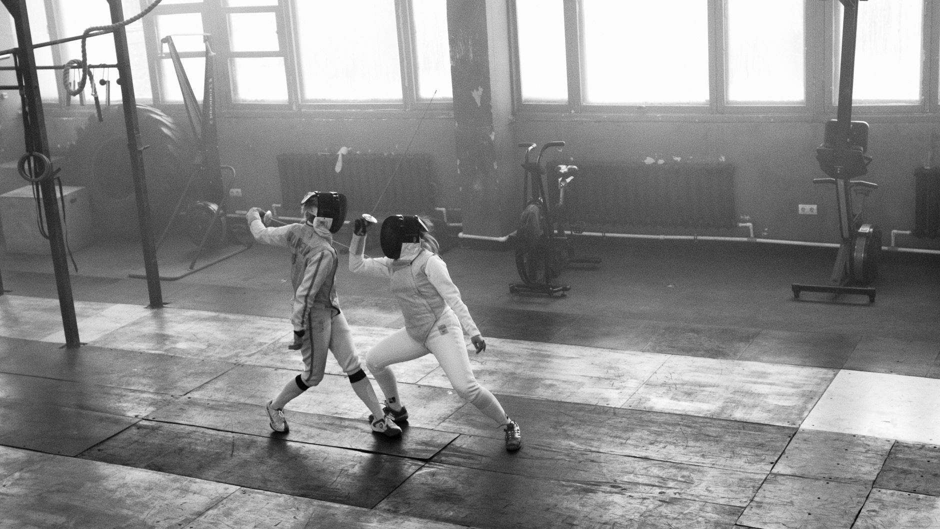 Two fencers engage in a dynamic duel indoors, showcasing skill.