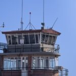 A modern airport control tower against a clear blue sky, showcasing aerial communication infrastructure.