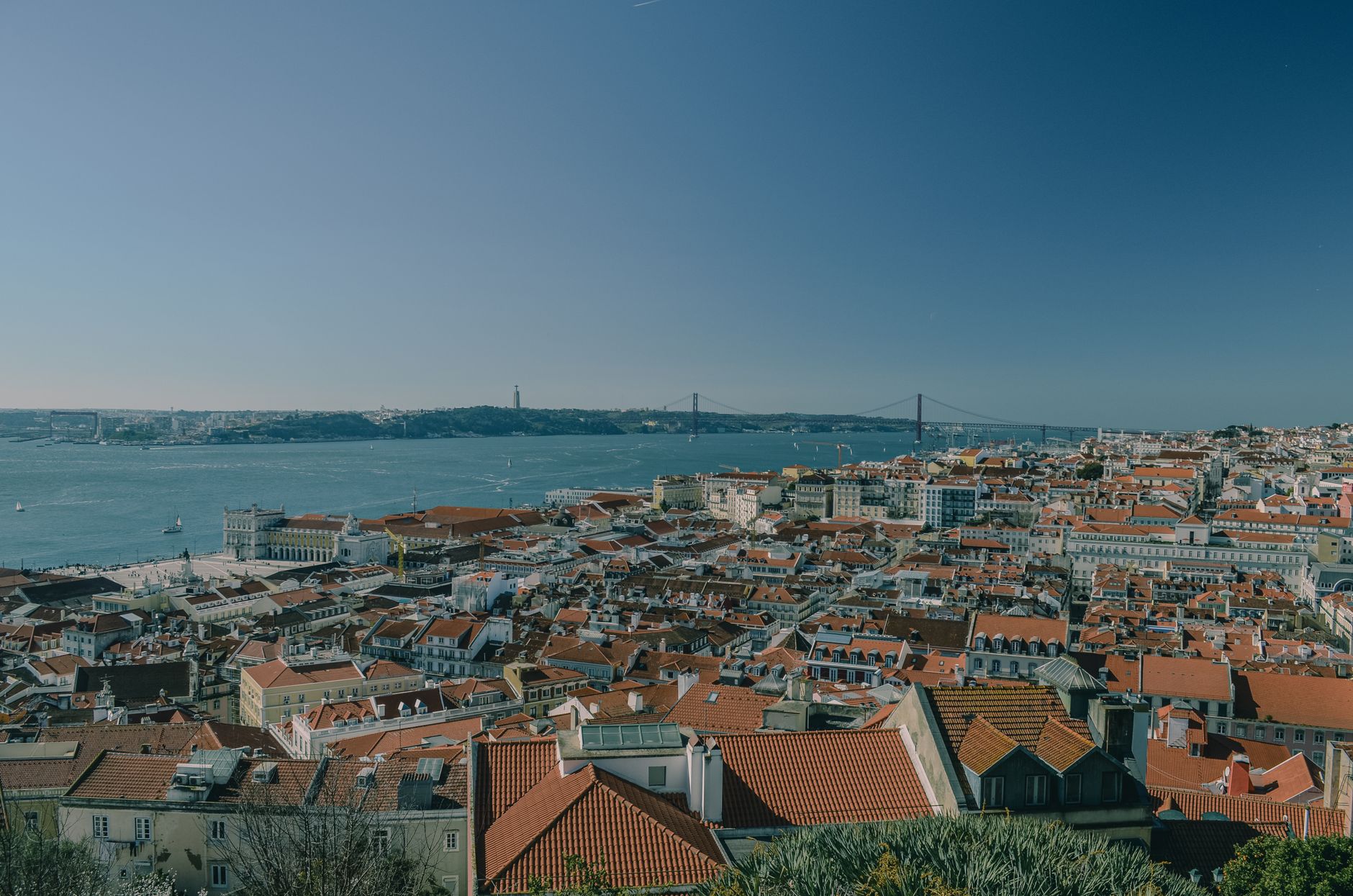 Scenic view of Lisbon's red rooftops and the Tagus River with the iconic 25 de Abril Bridge.