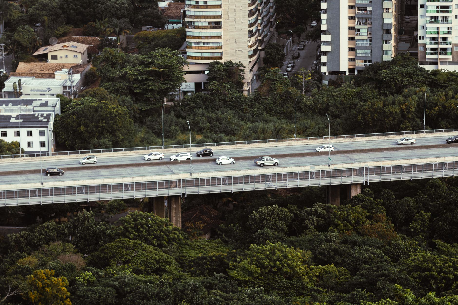 Overhead view of cars on a highway surrounded by urban buildings and lush greenery in Brazil.