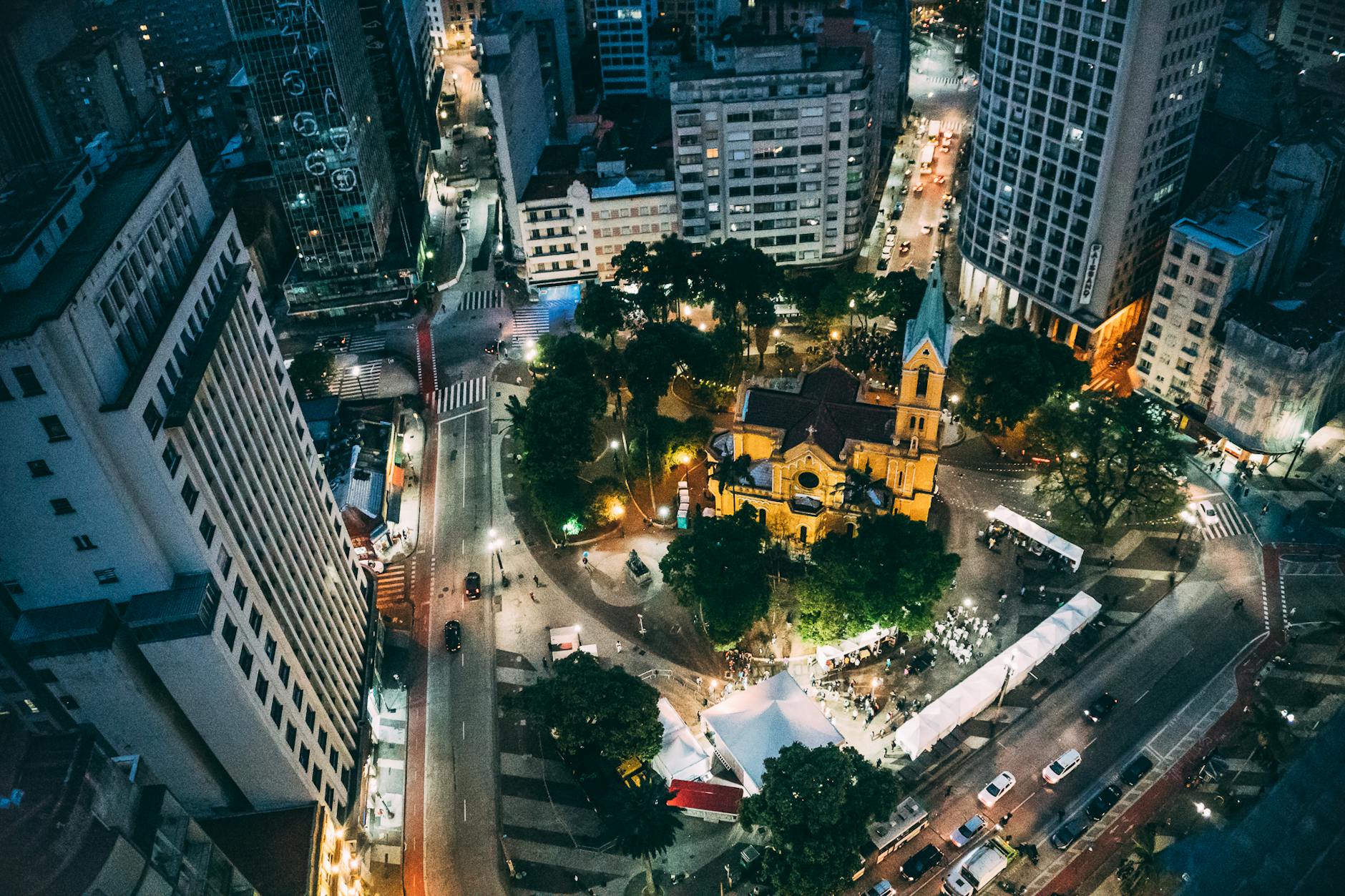 Aerial view of an illuminated cityscape highlighting a central plaza and church at night.