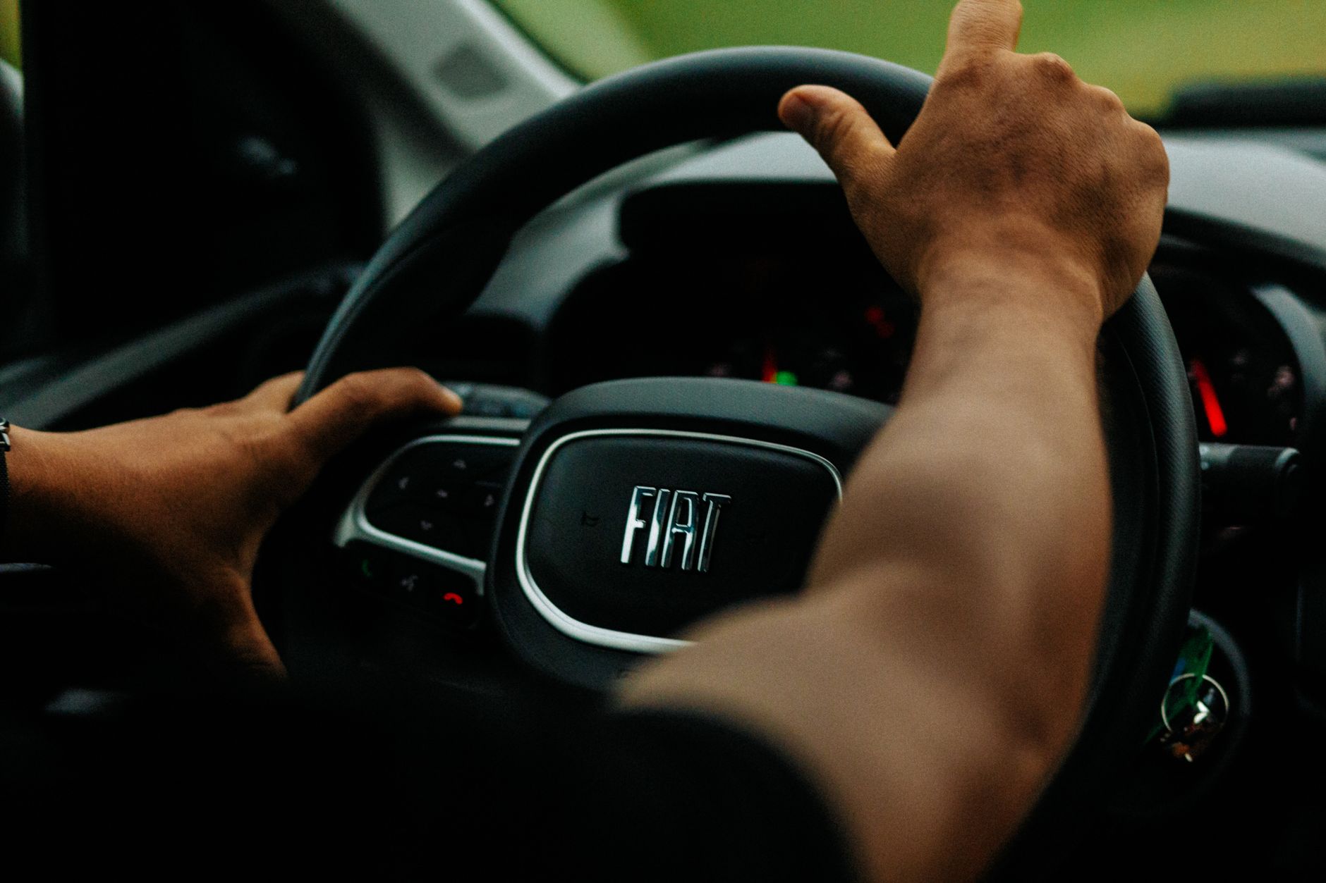 Detailed view of a man's hands on a Fiat steering wheel inside a vehicle.