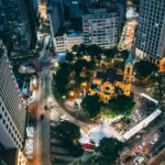 Aerial view of an illuminated cityscape highlighting a central plaza and church at night.