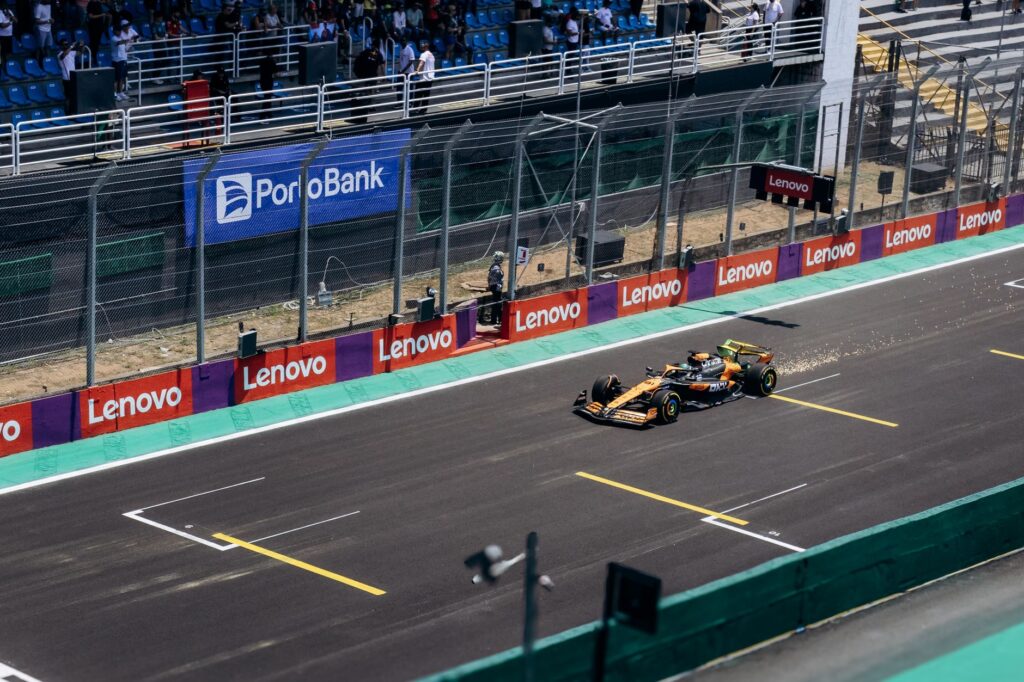 A Formula One car speeds past the grandstand during a daytime race at an outdoor track.