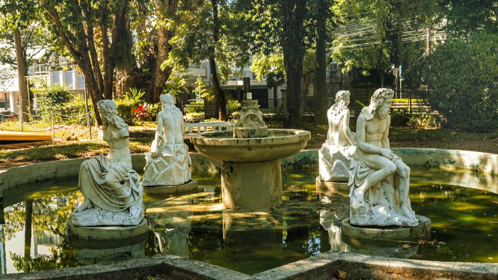 Elegant white statues encircle a fountain in a peaceful outdoor garden.