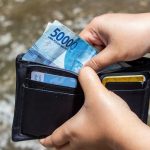 Close-up of hands inserting Indonesian Rupiah into wallet outdoors.