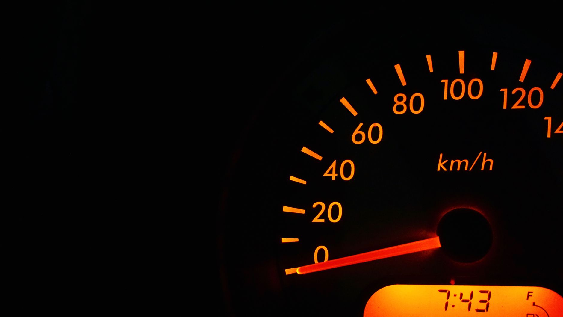 Night view of a car speedometer illuminated in orange, showing kilometers per hour.