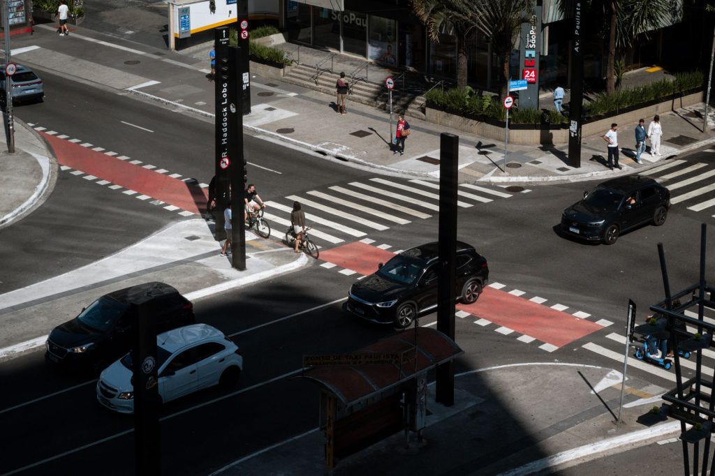 Dynamic aerial photo of an urban intersection in São Paulo with cars, cyclists, and pedestrians.