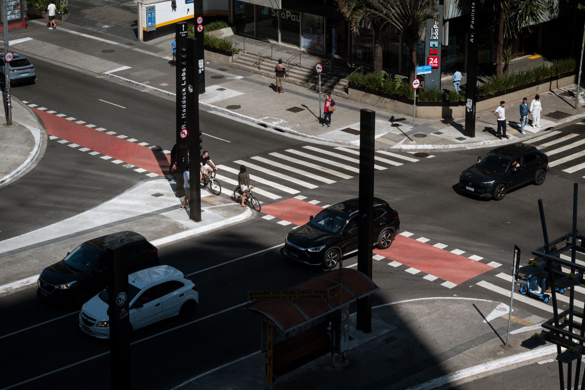 Dynamic aerial photo of an urban intersection in São Paulo with cars, cyclists, and pedestrians.