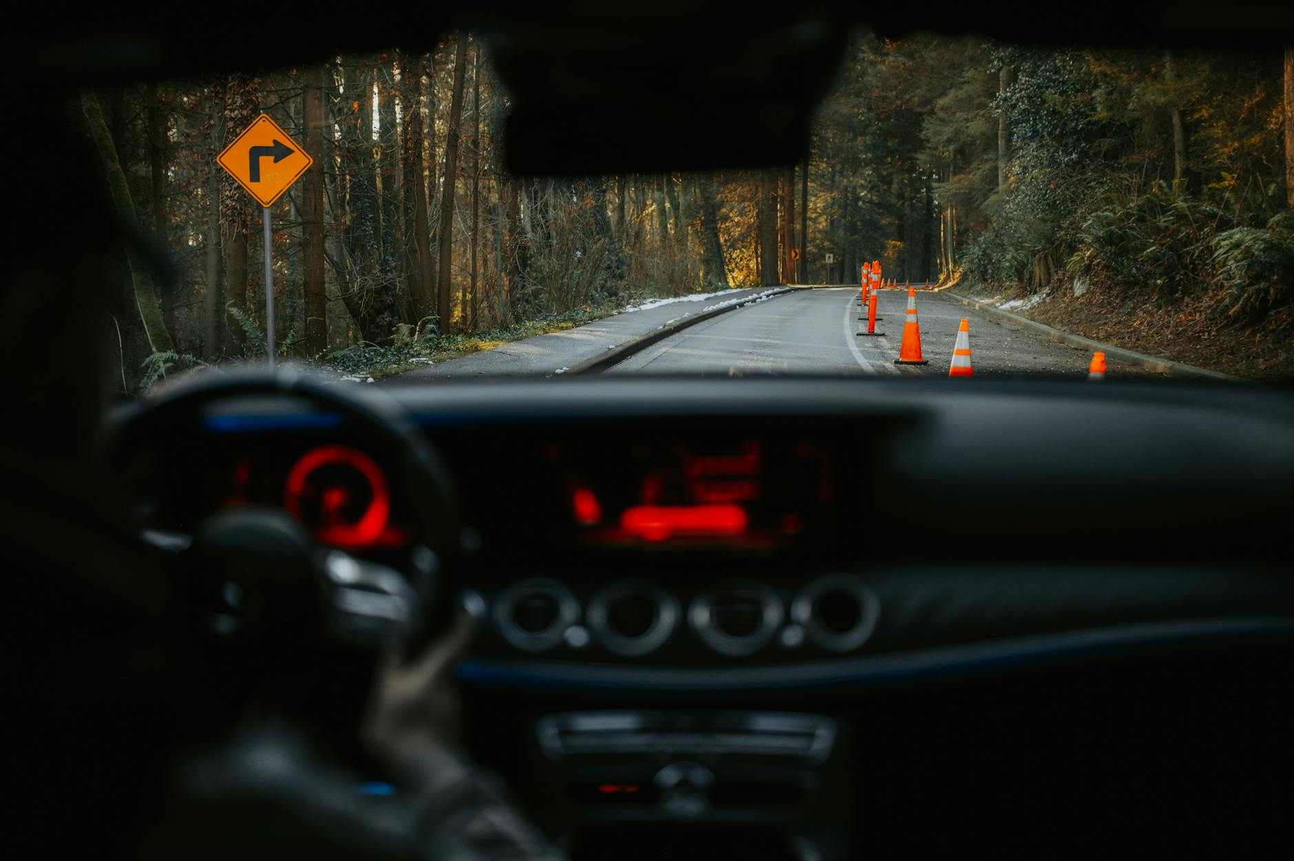View from car dashboard of rural road with traffic cones and turn sign. Scenic forest driving experience.