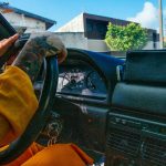 Close-up of a tattooed person driving a vintage car with a colorful dashboard.