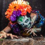Day of the Dead portrayal with skeletal makeup and bright floral headdress in Mexico City cemetery.
