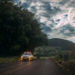 A police car drives on a rural road against a scenic twilight sky.