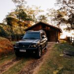 A black SUV parked outside a rustic cabin in the scenic countryside during sunset.
