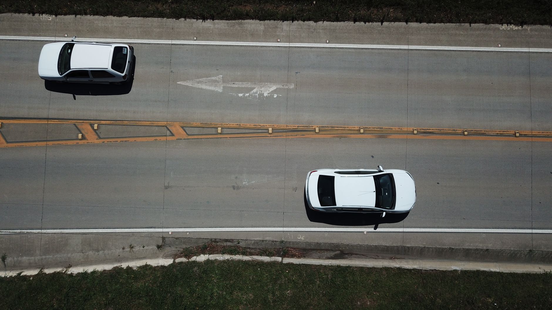 Aerial shot of two white cars on a highway with directional markings.