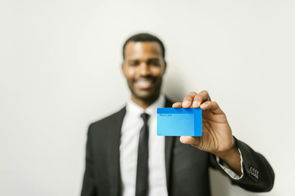Smiling businessman in a suit presenting a blue credit card against a neutral background.