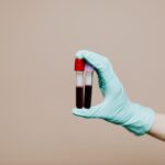 Close-up of a gloved hand holding two blood sample tubes in a laboratory setting.