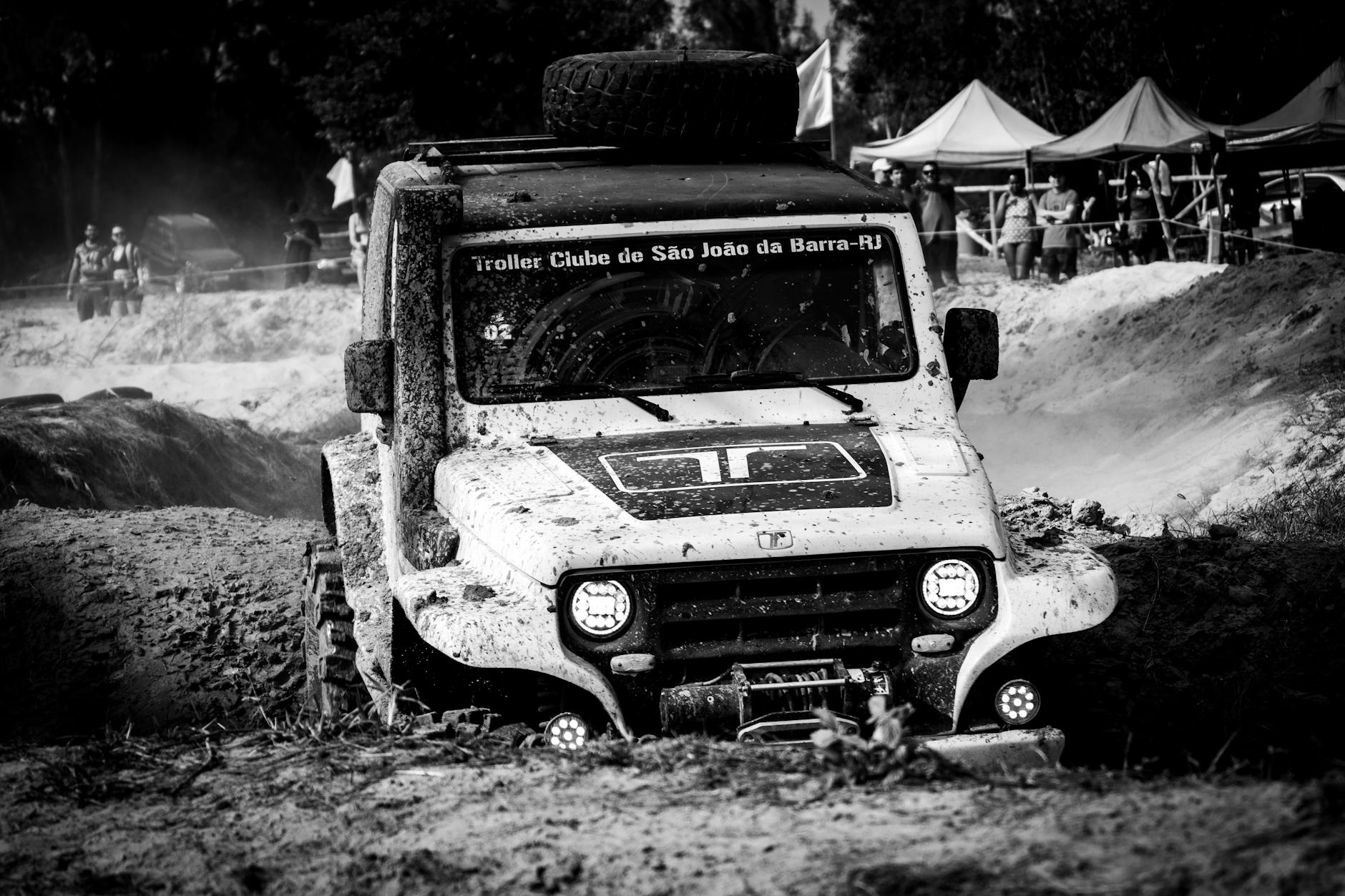 Black and white photo of a Jeep tackling muddy off-road terrain during a rally event.