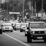 A busy city street scene with various cars in motion, captured in black and white.