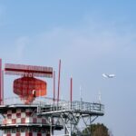 Radar tower and airplane in a blue sky, showcasing aviation technology