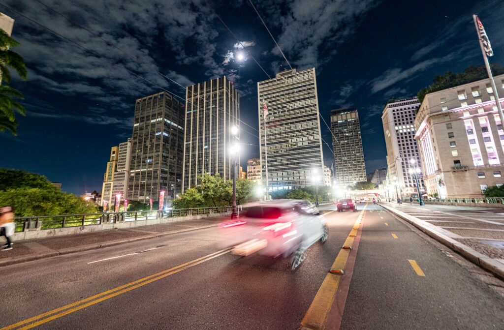Urban scene at night showcasing tall buildings and motion blur of a car on a city street.