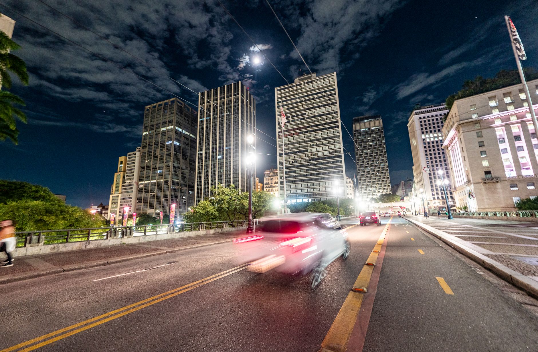 Urban scene at night showcasing tall buildings and motion blur of a car on a city street.