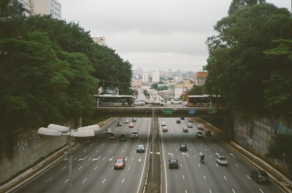 From above of busy asphalt road with cars and vehicles between lush green trees behind concrete walls