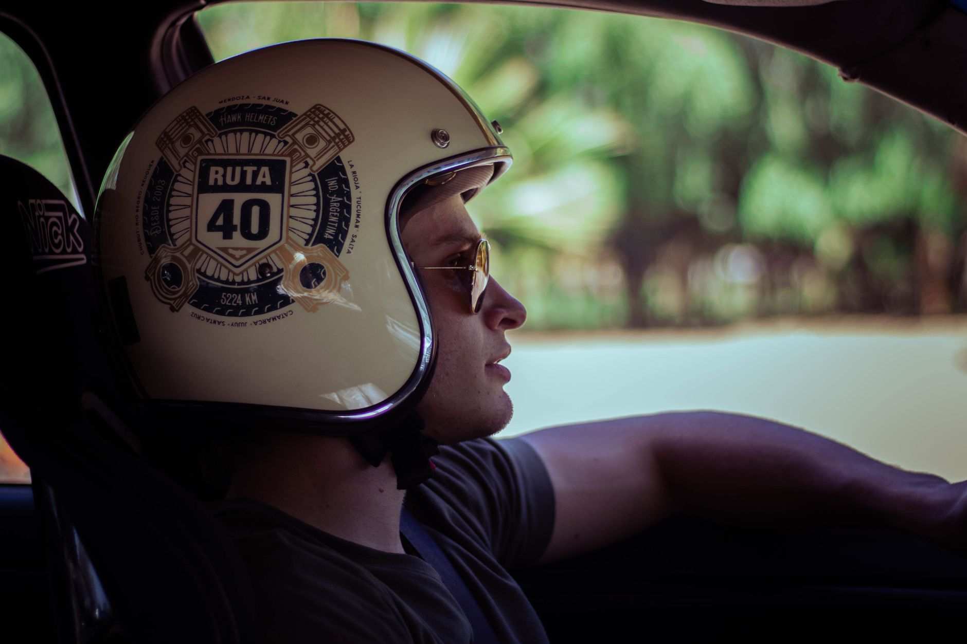 Side profile of a man driving, wearing a Ruta 40 helmet and sunglasses.