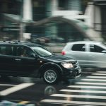 Vehicles speeding through a city street with a visible zebra crossing and blurred motion effect.
