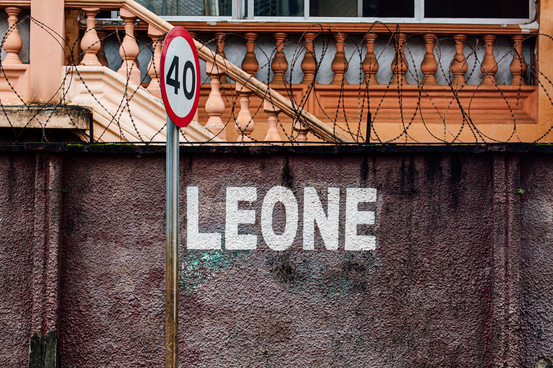 Photo of a 40 speed limit sign on a wall with 'LEONE' text and barbed wire.