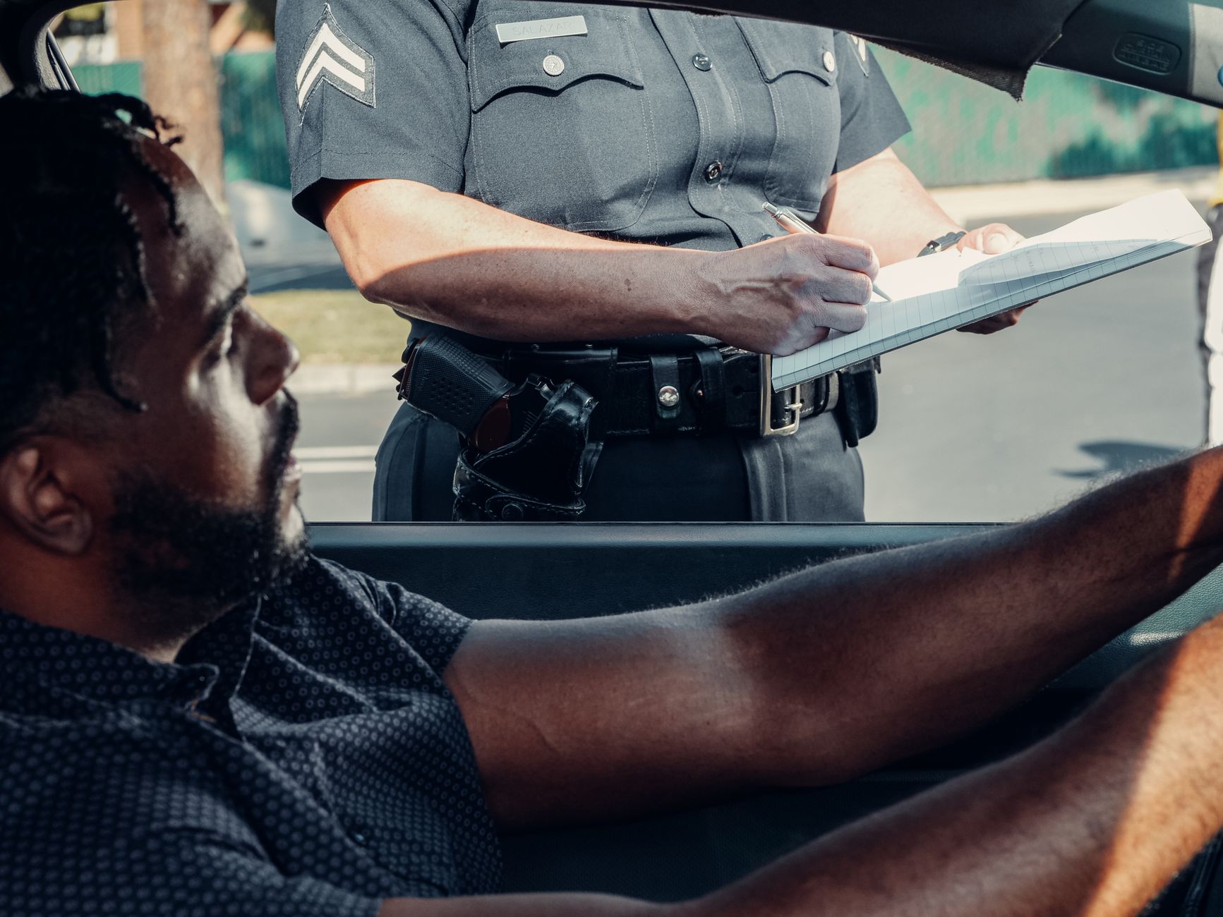 A police officer issues a traffic ticket to a driver seated in a car during the day.