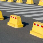 Yellow concrete barriers on asphalt next to a zebra crossing, emphasizing urban street safety.
