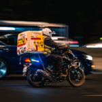 A delivery motorbike speeds through the streets of Kuwait City at night, showcasing fast-paced urban life.