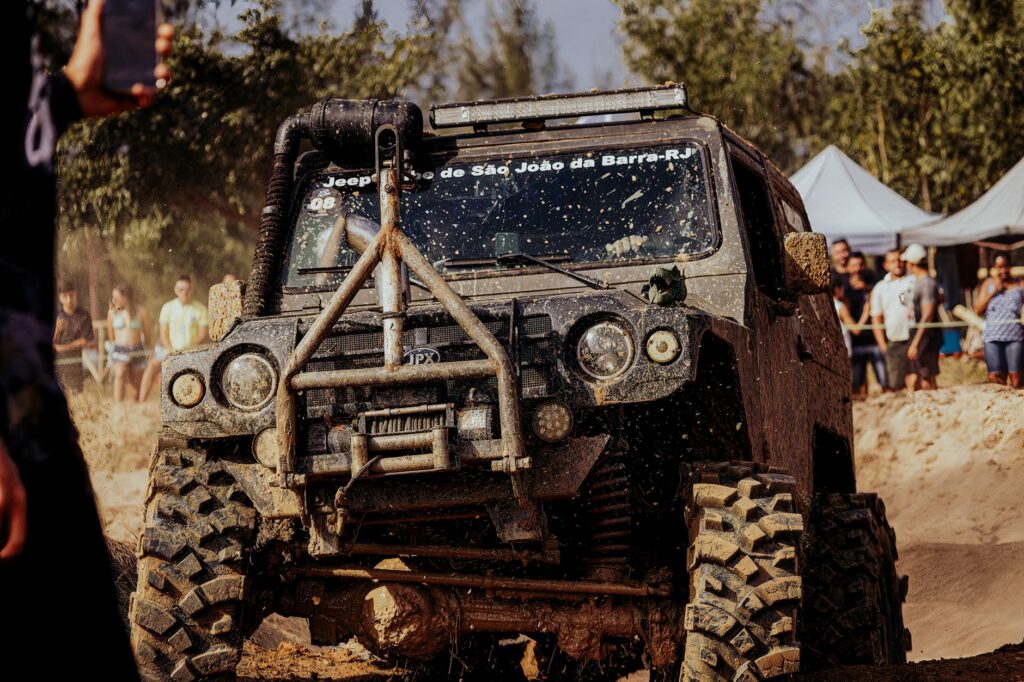 Jeep overcoming muddy terrain at off-road event with spectators watching in the background.