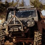 Jeep overcoming muddy terrain at off-road event with spectators watching in the background.