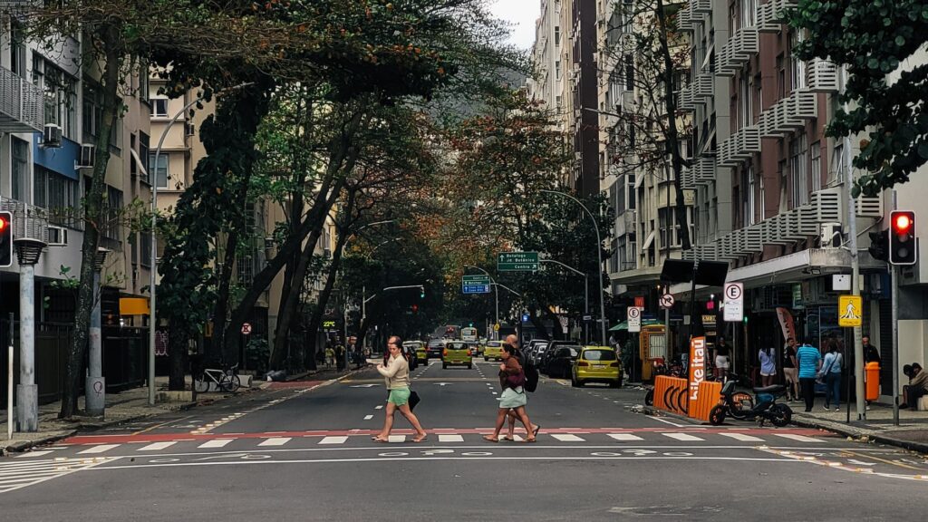 People crossing a street in Copacabana, Rio de Janeiro, surrounded by urban architecture.