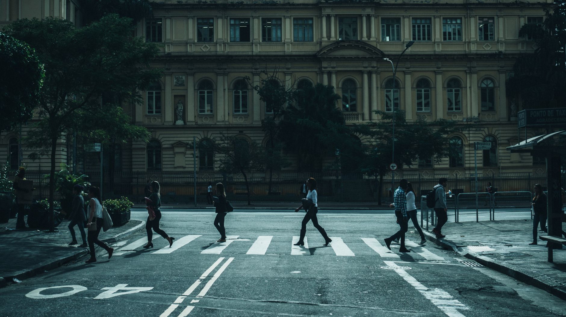 People crossing street in front of a historic building in urban setting.