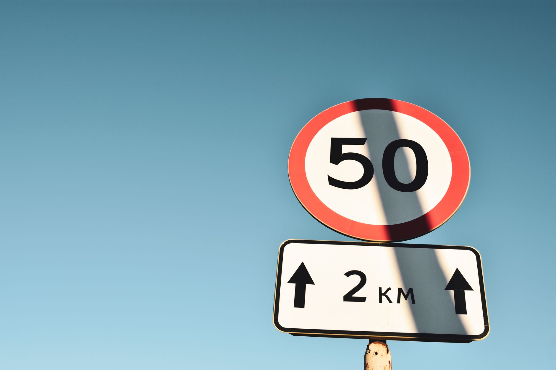 Clear speed limit and distance sign against blue sky, offering guidance and information.
