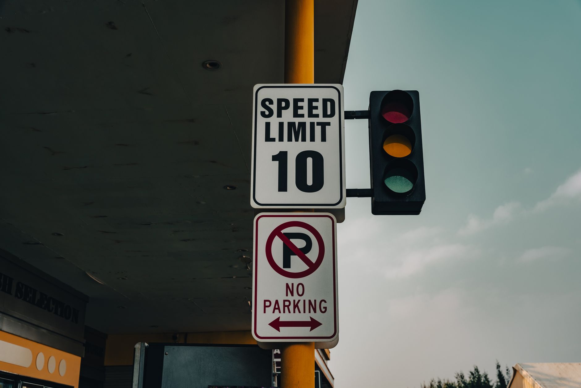 Close-up of a speed limit sign and traffic lights at an intersection under a cloudy sky.