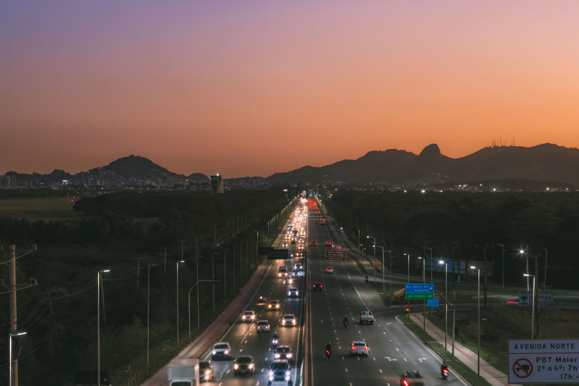 Captured aerial view of a busy highway with city skyline and mountains at sunset.
