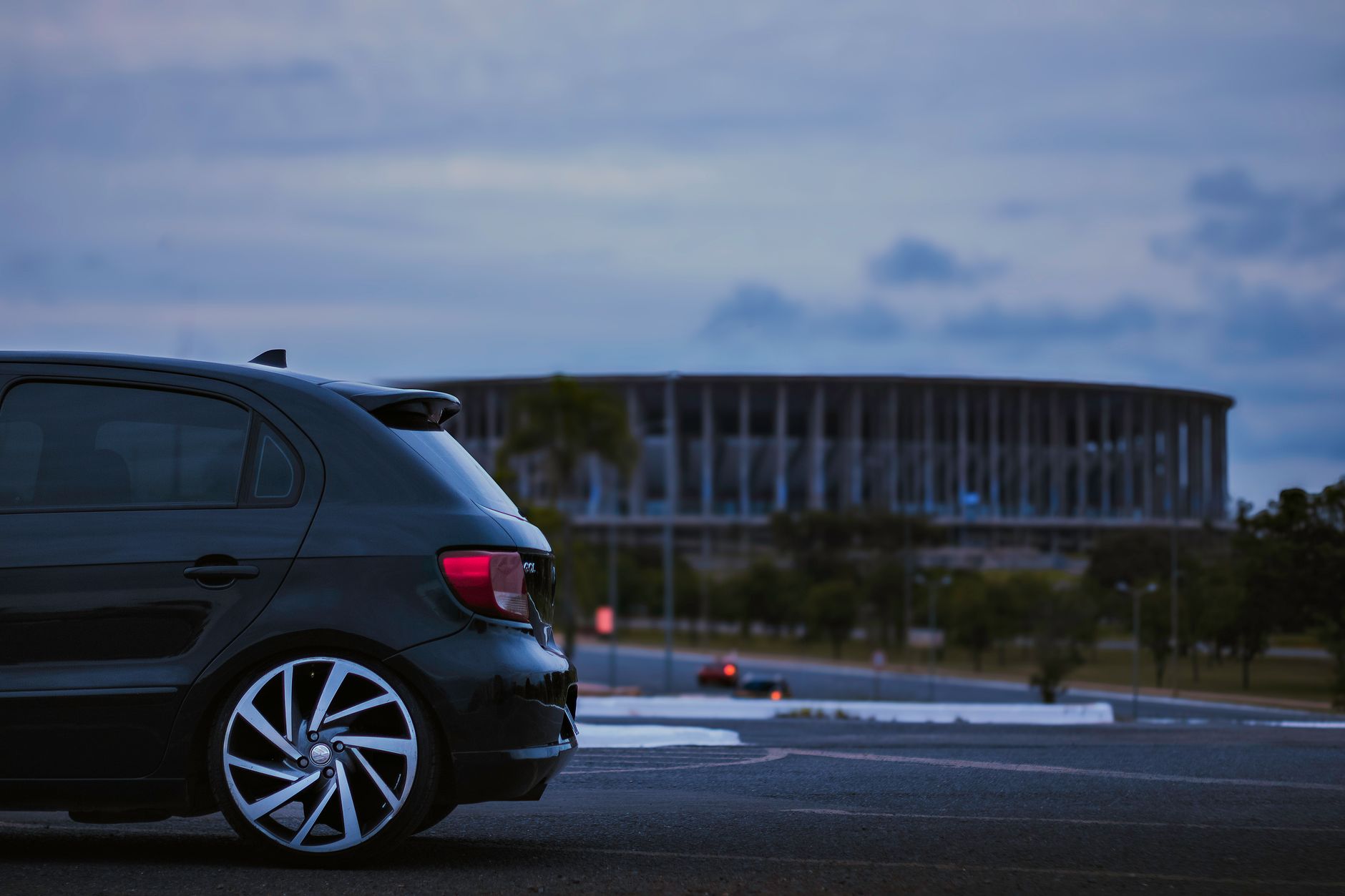 A black car parked near the iconic Estádio Nacional in Brasília at twilight.