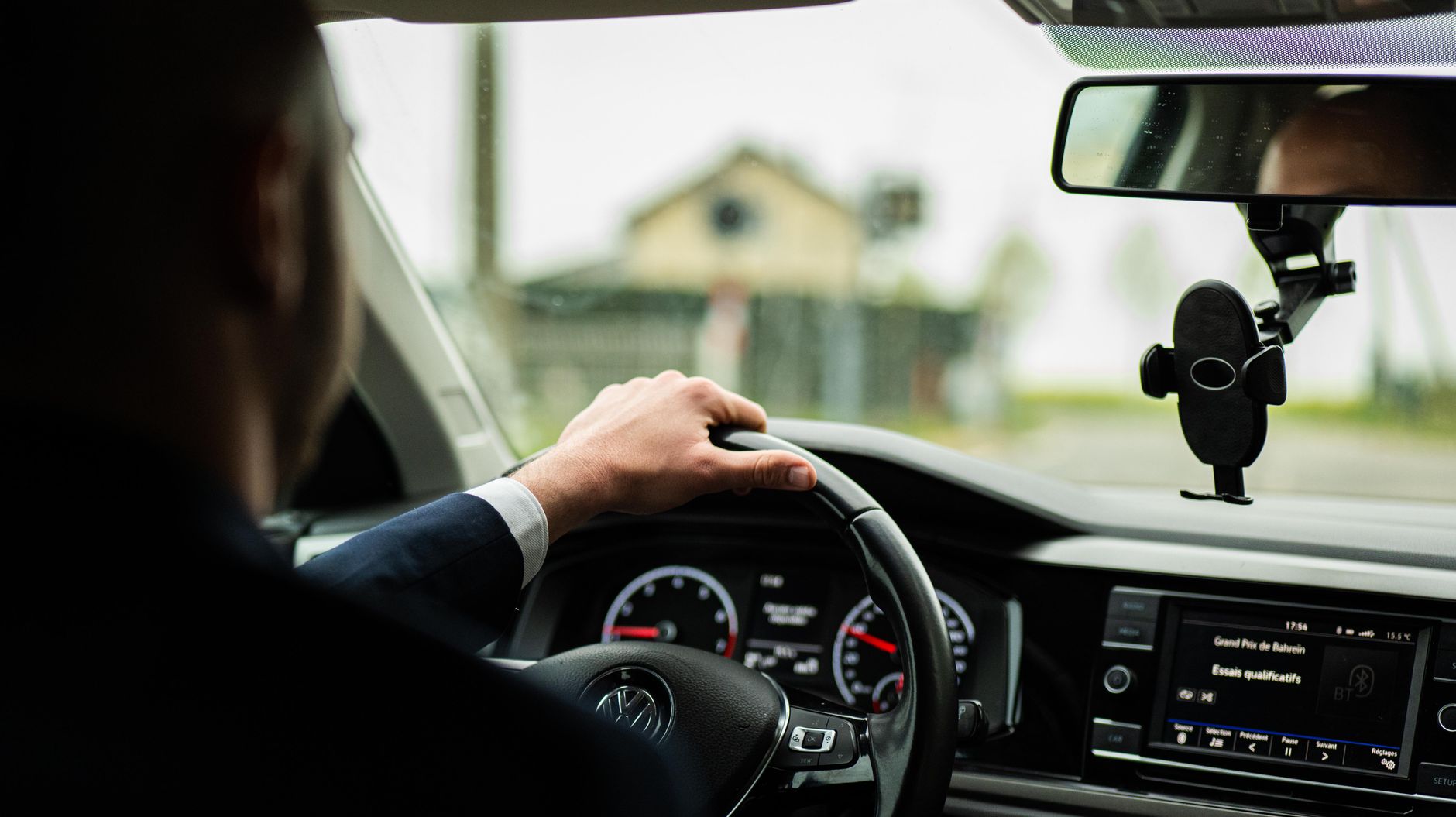 Businessman in suit driving a car, focus on steering wheel and dashboard.