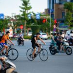 Cyclists and motorcyclists navigate a busy urban intersection on a sunny day, showcasing city life.