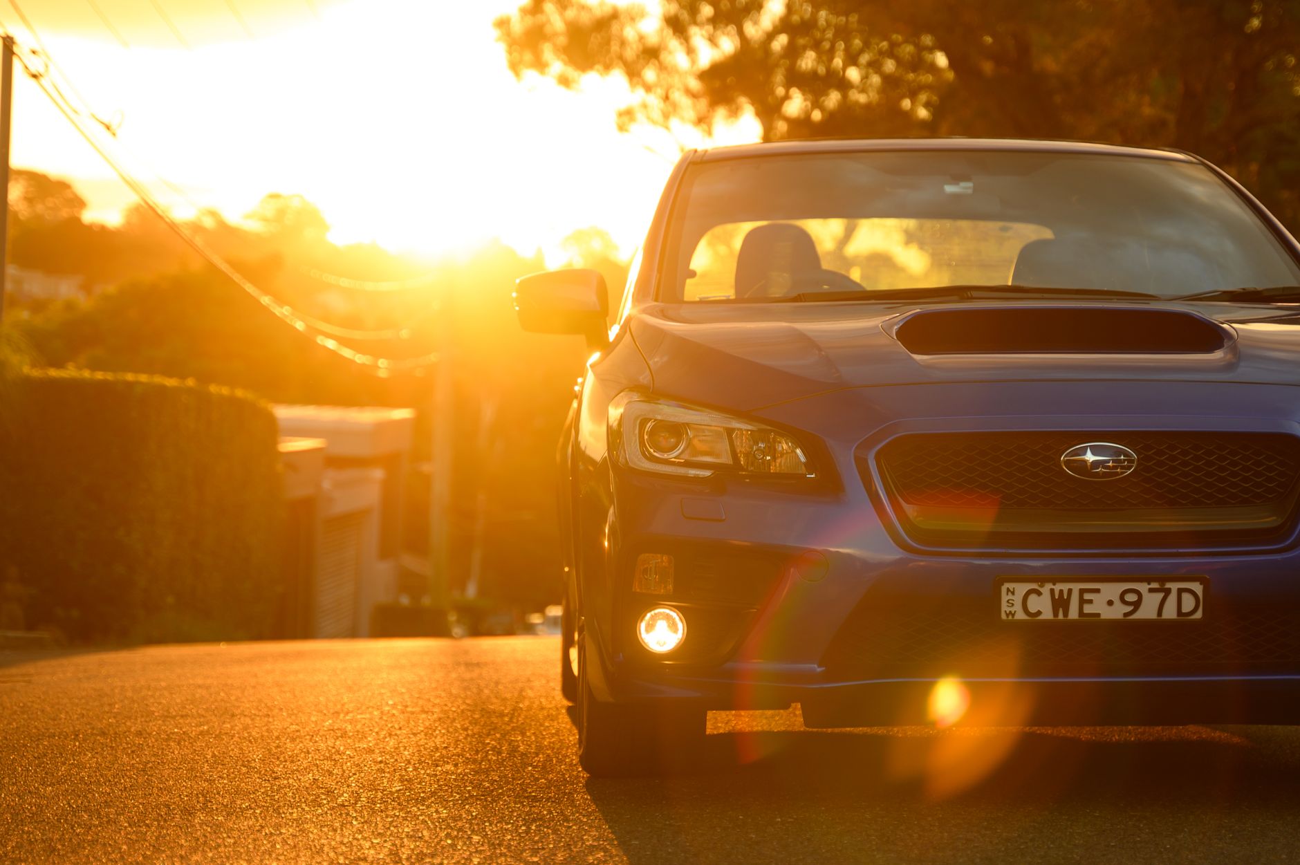 A blue Subaru WRX parked on a Sydney street during a scenic sunset, casting warm golden hues.