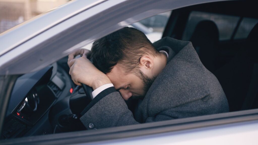 Man in car showing stress with head on steering wheel, highlighting emotional fatigue.