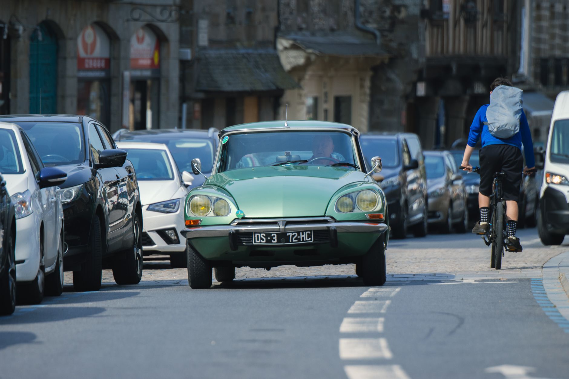 A classic car passes a cyclist on a street in Dol-de-Bretagne, France.