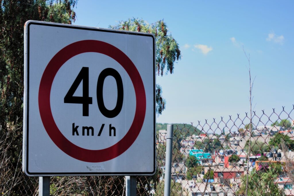 Close-up of a 40 km/h speed limit sign near a chain-link fence and urban landscape.